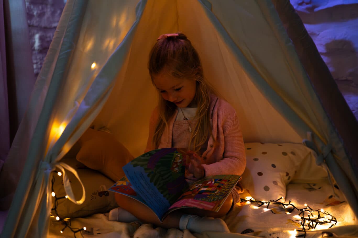 Child reading a book in the children's bedroom teepee with fairy lights